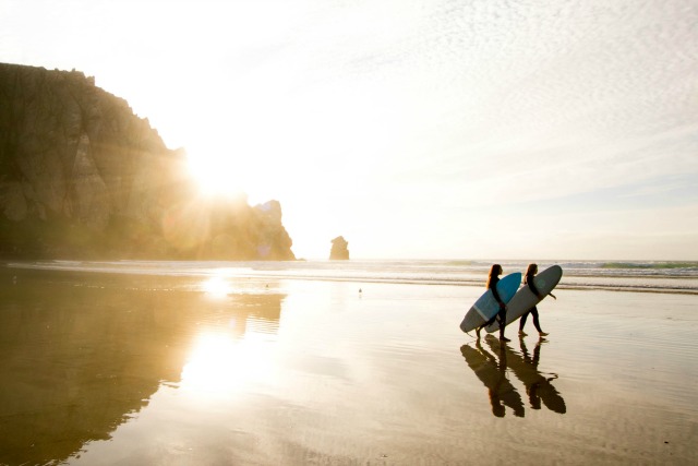 Surfers going out to catch a wave near sunset. Try these 20 passive income ideas to build wealth and options into your life. 