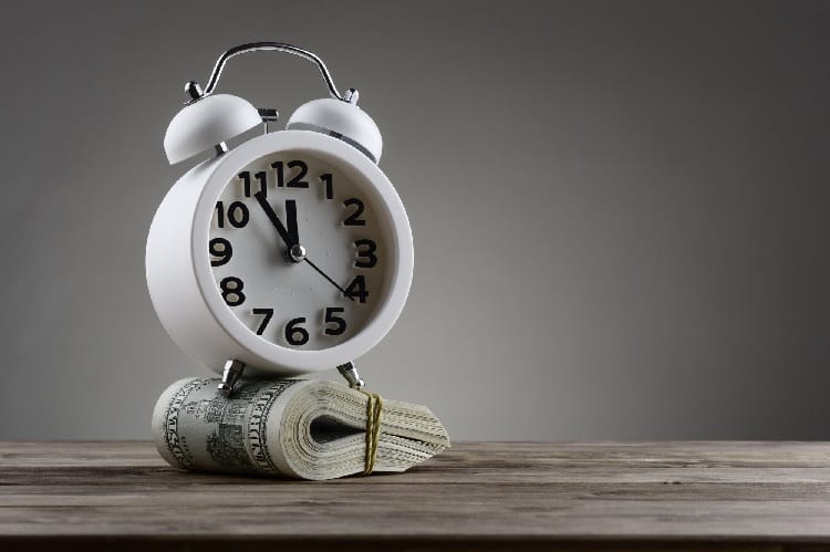 Image of a clock on top of a wad of cash. Time and Money.