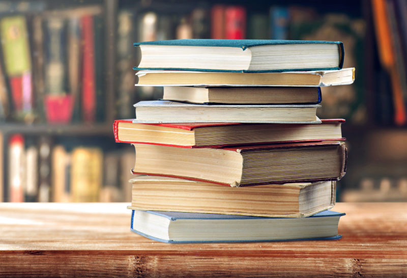 Stack of eight books on a weathered table. 